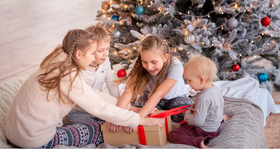 Kids opening a present in the family room next to a Christmas tree.